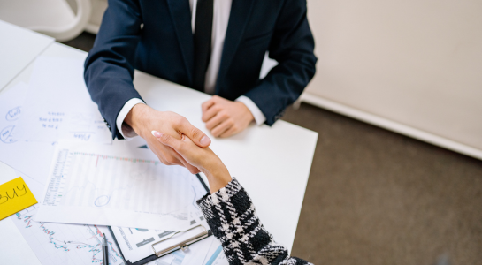 Business professionals shaking hands over documents on an office desk.