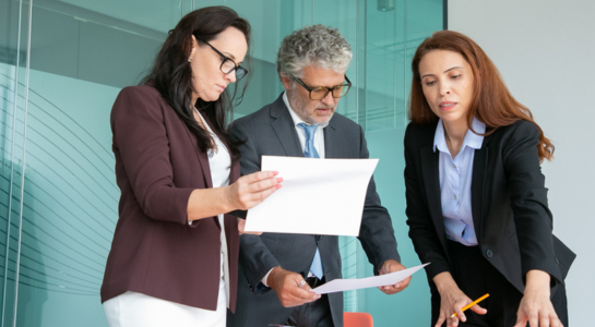 Three professionals reviewing documents together in an office meeting.