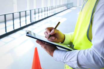 Safety inspector in a high-visibility vest writing notes on a clipboard.