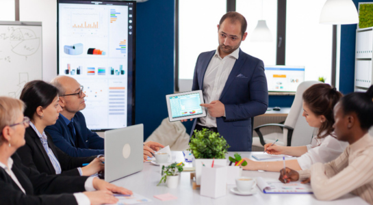Manager presenting data on a tablet to a team during a business meeting.