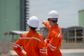 Two construction workers in safety gear discussing work at an industrial site.