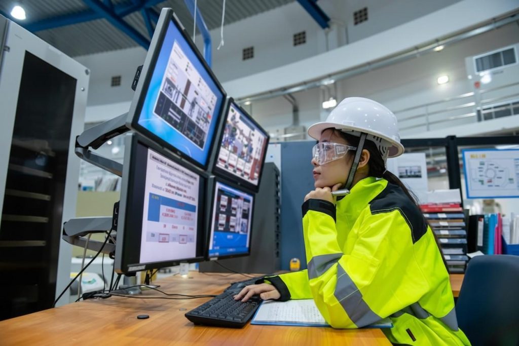 Engineer monitoring multiple computer screens in an industrial control room.